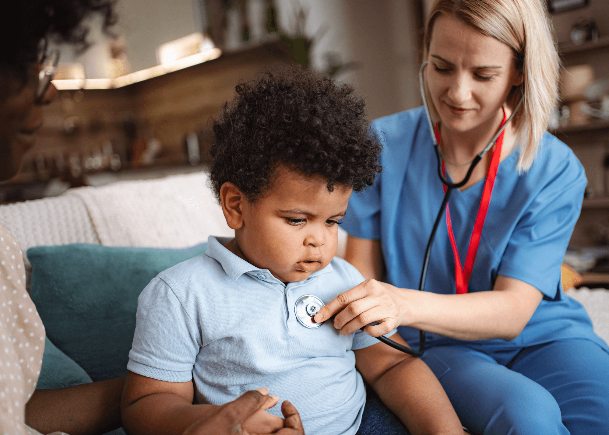 Nurse in blue scrubs examining a young child with a stethoscope during a home visit